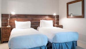 Habitación de hotel con dos camas, cabecera de madera, lámparas de noche, una mesita de noche y un espejo en la pared.