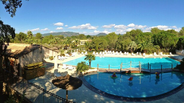 A resort with a large swimming pool surrounded by lounge chairs and umbrellas, set against a backdrop of trees and mountains.