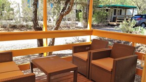 A wooden deck with wicker furniture, including a table and chairs, overlooking a parking area with a vehicle and trees.