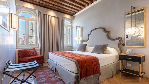 Un dormitorio con una cama grande, una mesita de noche de madera, una silla roja y una ventana con cortinas.