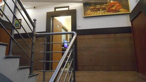 A staircase with metal railings leading to a room with wooden paneling and a framed picture on the wall. - Hotel Aditya Mysore (Mysore)