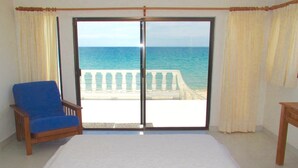 Quarto com uma cama grande, uma cadeira azul e vista para o mar através de uma porta de correr.