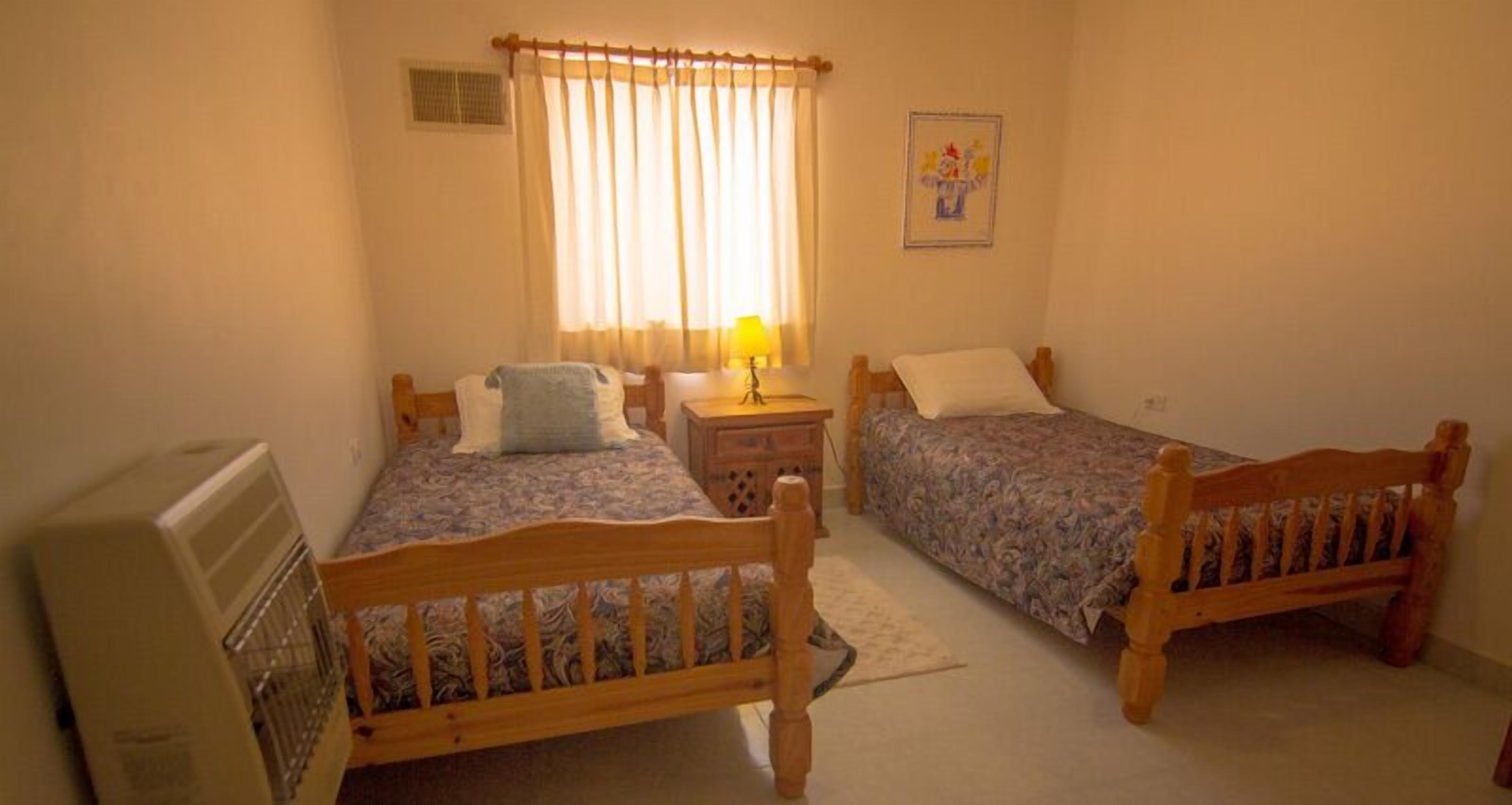 Une chambre à coucher avec deux lits en bois, une table de chevet avec une lampe, un radiateur et une fenêtre avec des rideaux.