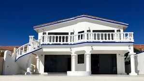 Um edifício branco com telhado azul, uma varanda e uma escadaria que leva à entrada.