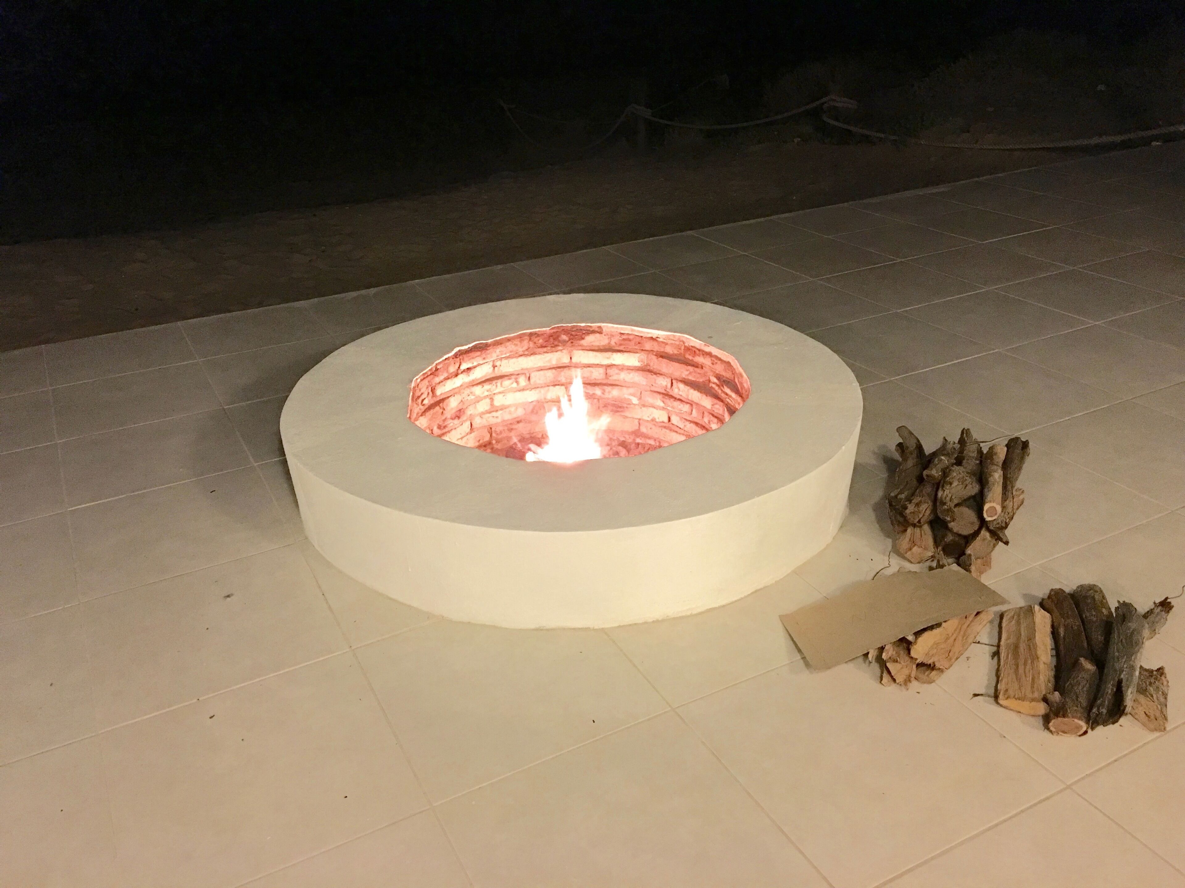 Pyöreä ulkotulisija, jossa näkyy liekki, ja jonka ympärillä on laatoitettu alue.