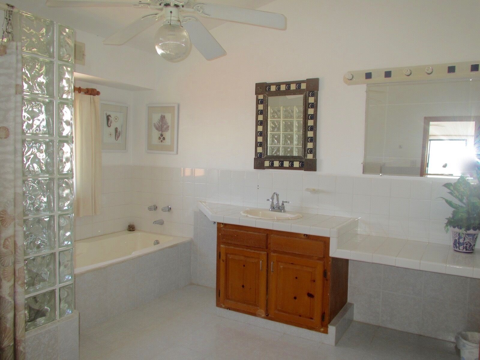 Un baño con bañera, lavamanos, armarios de madera, ventilador de techo y espejo.