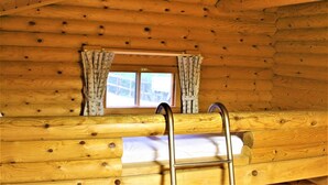L’intérieur d’une cabane en bois, avec un lit superposé, une fenêtre avec des rideaux et une échelle.