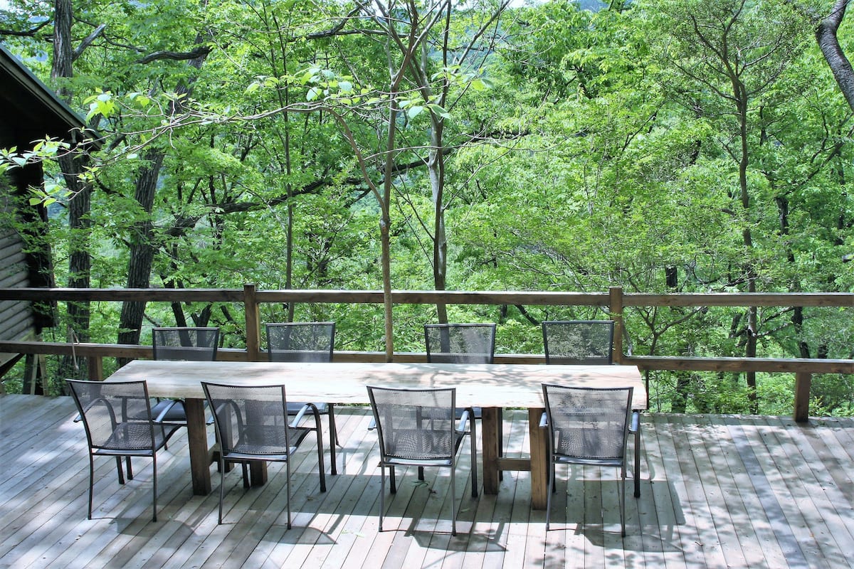 A wooden deck with a table and chairs, surrounded by a wooden railing, overlooking a forested area.