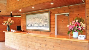 Un comptoir d’accueil en bois, orné d’un tableau encadré, d’un vase de fleurs et d’un panneau indiquant l’emplacement du bureau d’accueil.