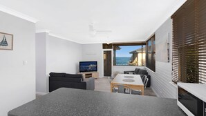 A compact living space with a dining area, a TV, and a view of the sea. - Golden Sands Apartment 10 (Blue Bay)