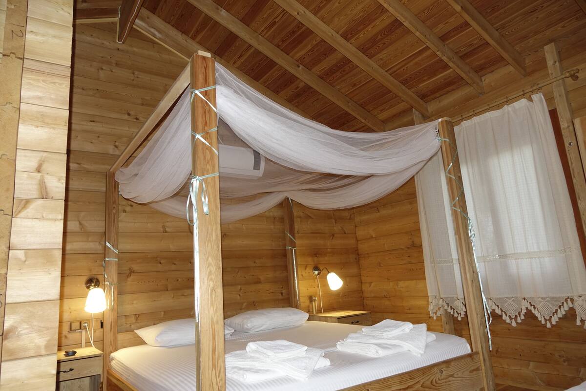 Una habitación de cabaña de madera con una cama con dosel, dos lámparas de noche y un dosel.