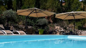 Ein Swimmingpool mit Liegestühlen und Sonnenschirmen, umgeben von Grünpflanzen und Felsen.