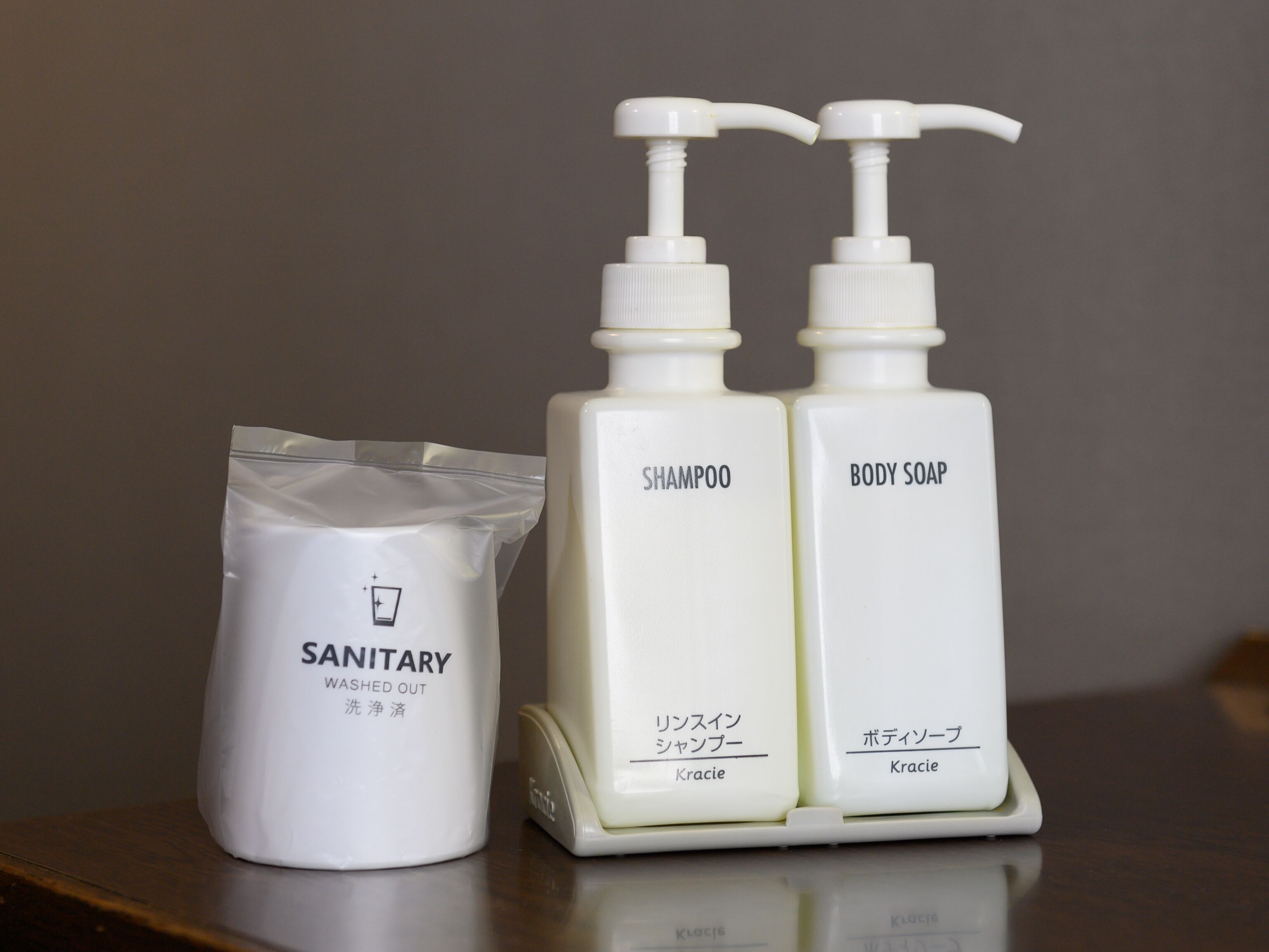 Two white bottles labeled 'SHAMPOO' and 'BODY SOAP' with pumps, and a white bag labeled 'SANITARY WASHED OUT'.