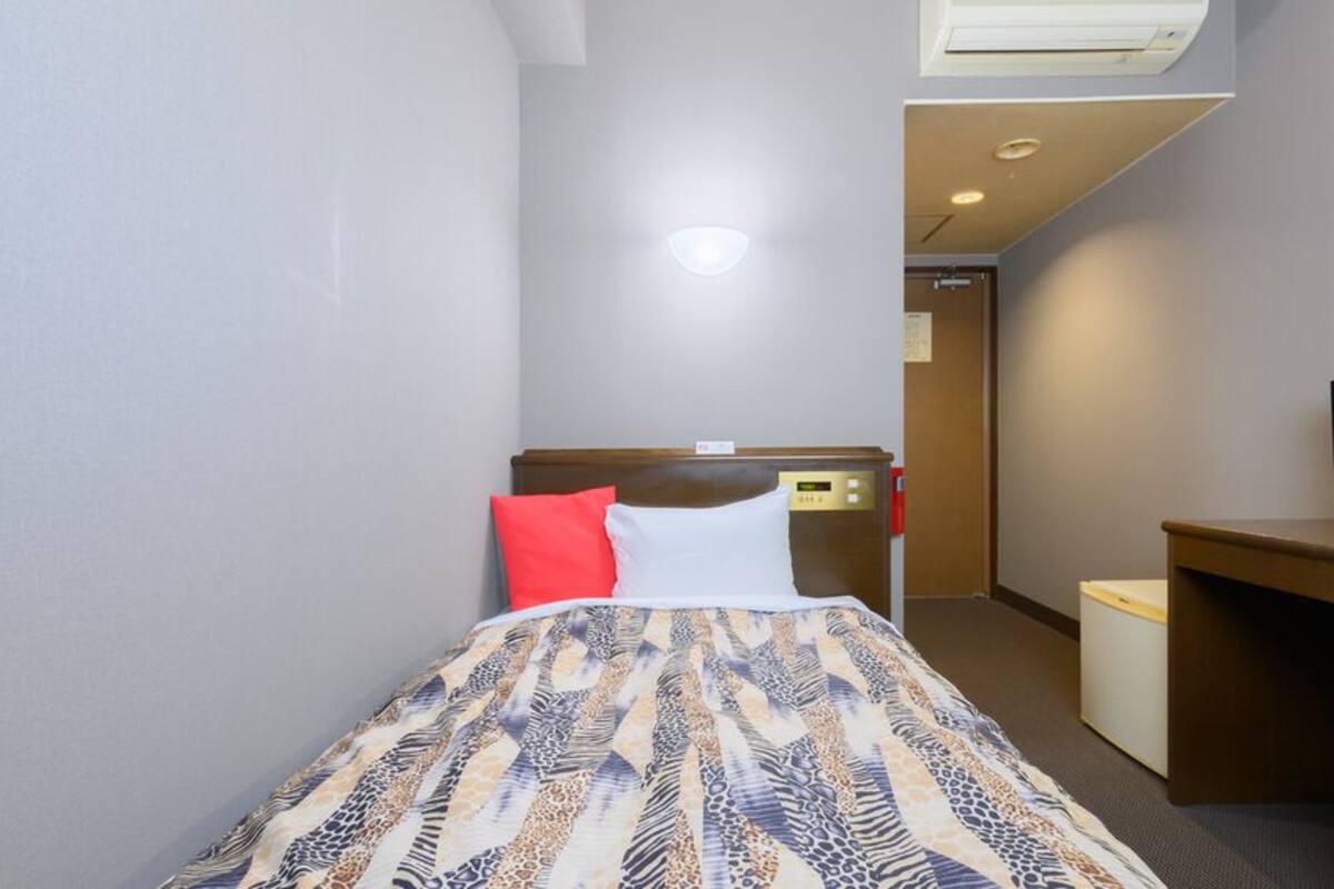 A hotel room with a bed, a desk, a television, and an air conditioning unit.