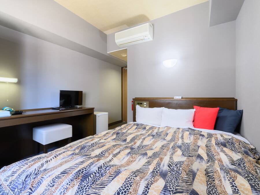 Una habitación de hotel con cama, escritorio, televisor y aire acondicionado.