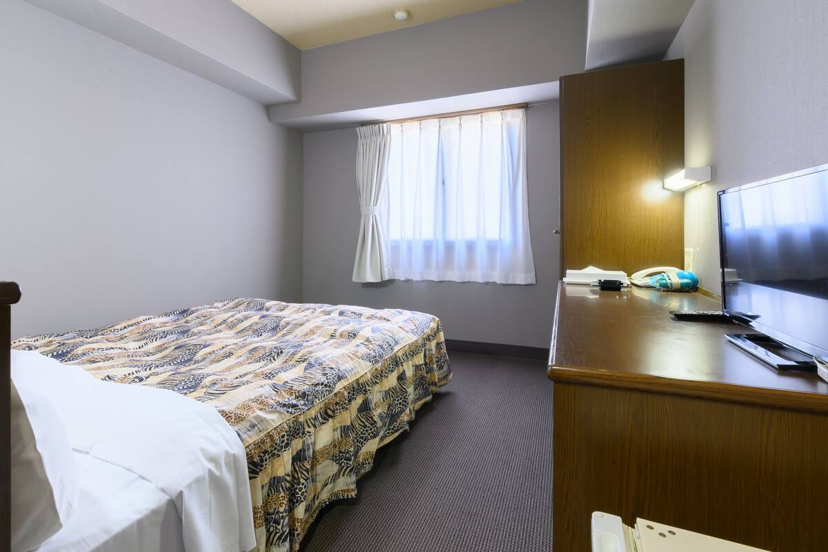 A hotel room with a bed, a desk, a television, and a window with curtains.