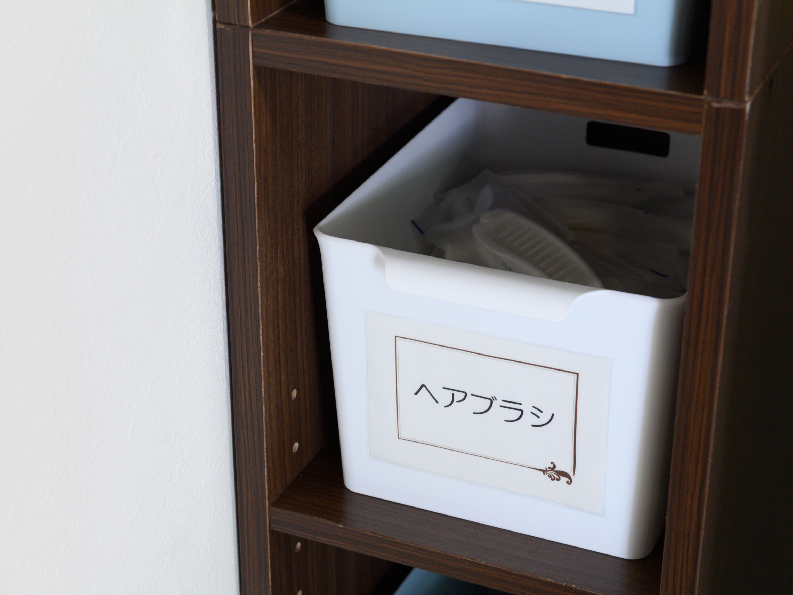 A white storage bin with a label in a foreign script, placed on a wooden shelf.
