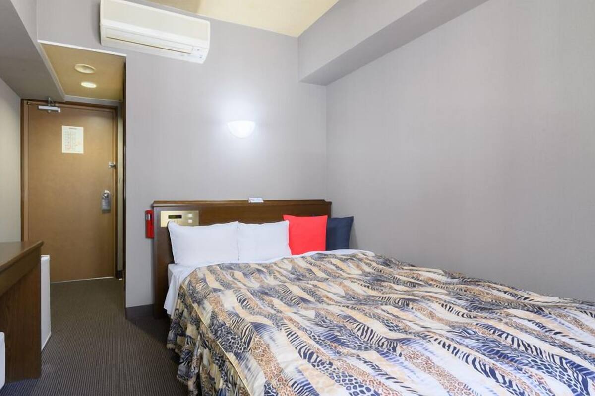 A hotel room with a bed, a desk, a television, and an air conditioning unit.