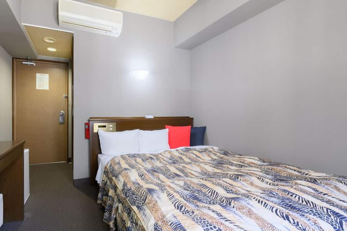 Una habitación de hotel con una cama, un escritorio, un televisor y un equipo de aire acondicionado.