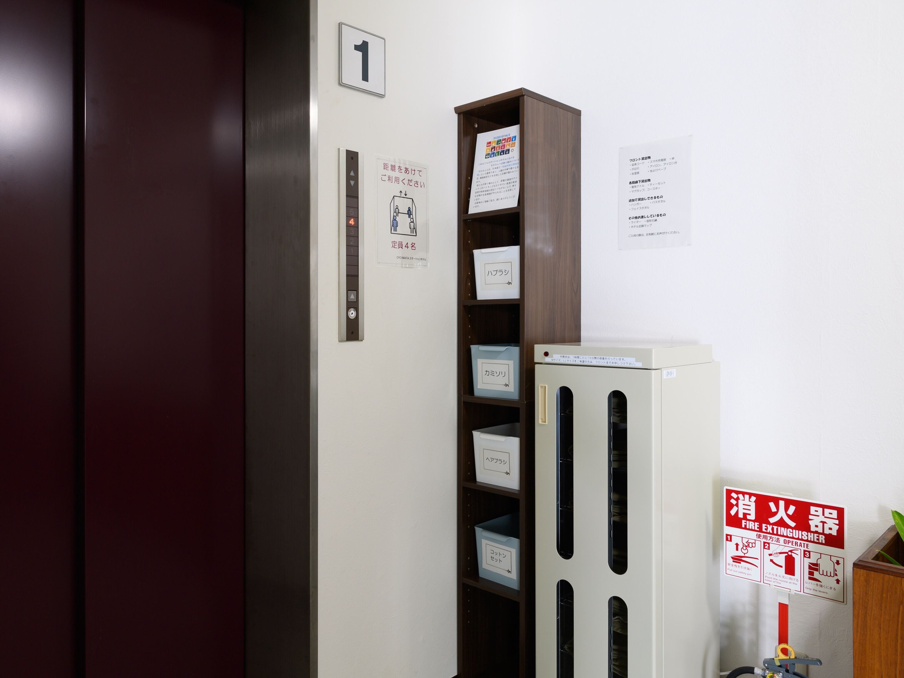 An elevator with a sign indicating it is the first floor, a fire extinguisher, and storage boxes labeled with different names.