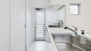 A modern kitchen with a stainless steel sink, a window, and a door leading to another room. - Niraikanai (Nanjo)