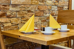 Une table en bois, avec un mur en pierre en arrière-plan, une paire de serviettes jaunes, ainsi que des tasses et des soucoupes blanches.
