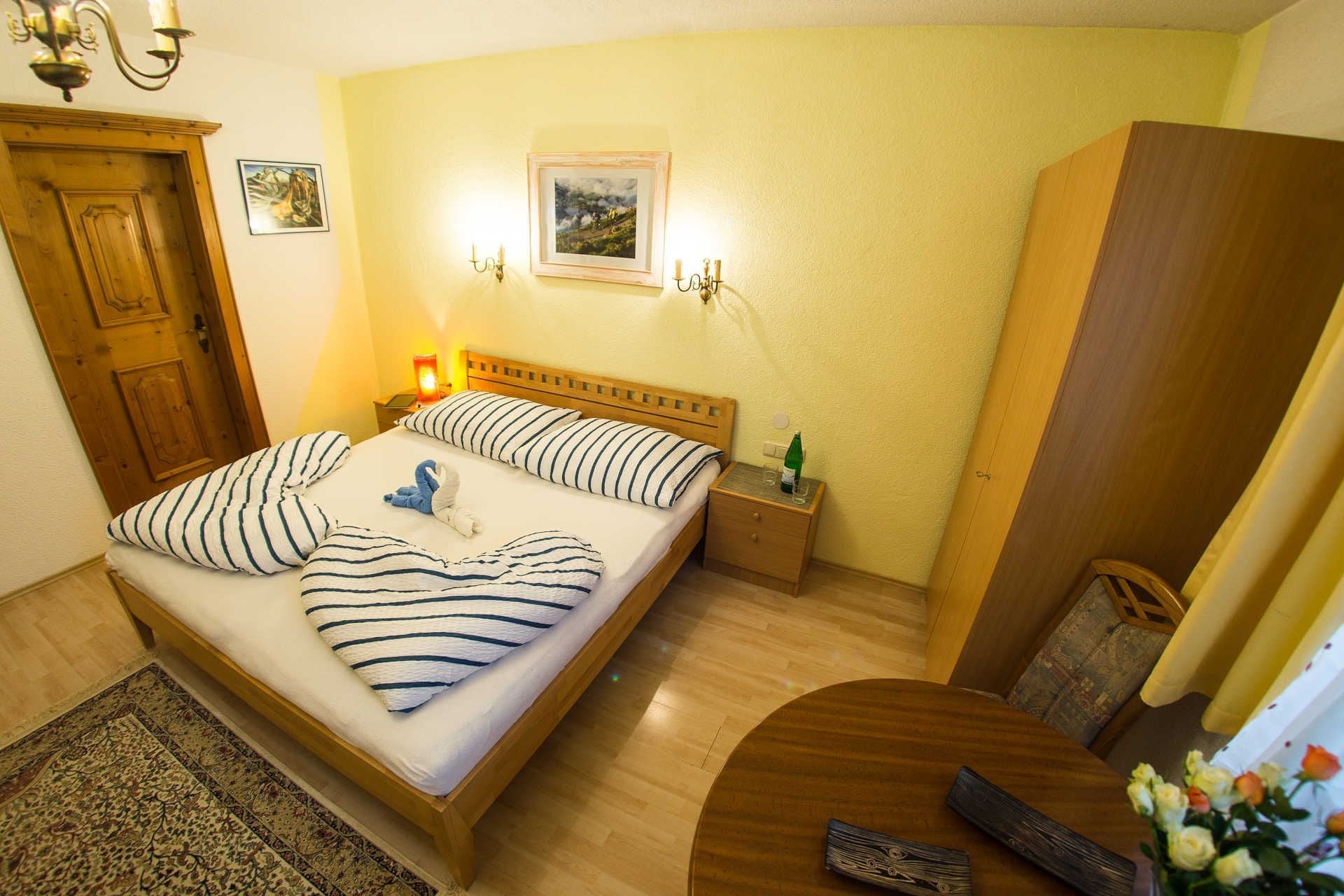 Une chambre d’hôtel avec un lit, des tables de chevet, une armoire en bois, une table ronde et une télécommande posée sur le sol.