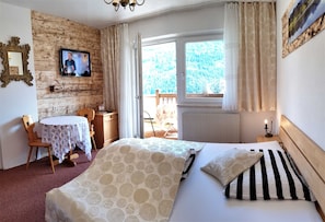 Une chambre d’hôtel avec un lit, une télévision, une petite table avec des chaises, une fenêtre avec des rideaux et une vue sur un balcon.
