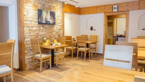 A dining area with wooden tables and chairs, a stone wall, and a television mounted above the wall. - Double bed room with breakfast - Europa Pension Tirol (Fließ)