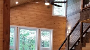 A spacious living room with a wooden ceiling, large windows, a sofa set, a television, and a staircase. - Storybook Caretaker's Cabin in the Woods -Clemson (Central)