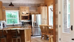 A spacious kitchen with wooden cabinets, a central island with stools, and a refrigerator. - Storybook Caretaker's Cabin in the Woods -Clemson (Central)
