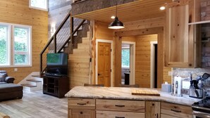 A wooden cabin interior with a living room, kitchen, and staircase. - Storybook Caretaker's Cabin in the Woods -Clemson (Central)