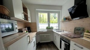 Een kleine keuken met een magnetron, fornuis, spoelbak en een raam met uitzicht op groen.