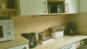 Een kitchenette met een magnetron, koffiezetapparaat en een mand met spullen op het aanrecht.