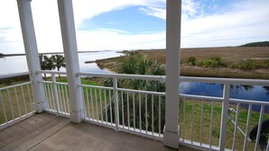Un balcon couvert, doté de balustrades blanches, qui offre une vue sur une étendue d’eau et un paysage verdoyant.