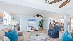 Ein geräumiges Wohnzimmer mit einer Couch, einem Sessel und einem Couchtisch, einem Fernseher und einer Küchenzeile im Hintergrund.