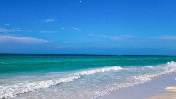 Ein Strand mit klarem türkisblauem Wasser, sanften Wellen und blauem Himmel.