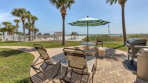 Ein Außenbereich mit Terrasse, Grill, Sitzgelegenheiten und Blick auf den Strand.