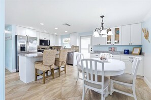 A modern kitchen with white cabinetry, a central island, and a dining area with white chairs.