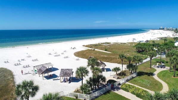 A beach with white sand, clear blue water, and a few palm trees.