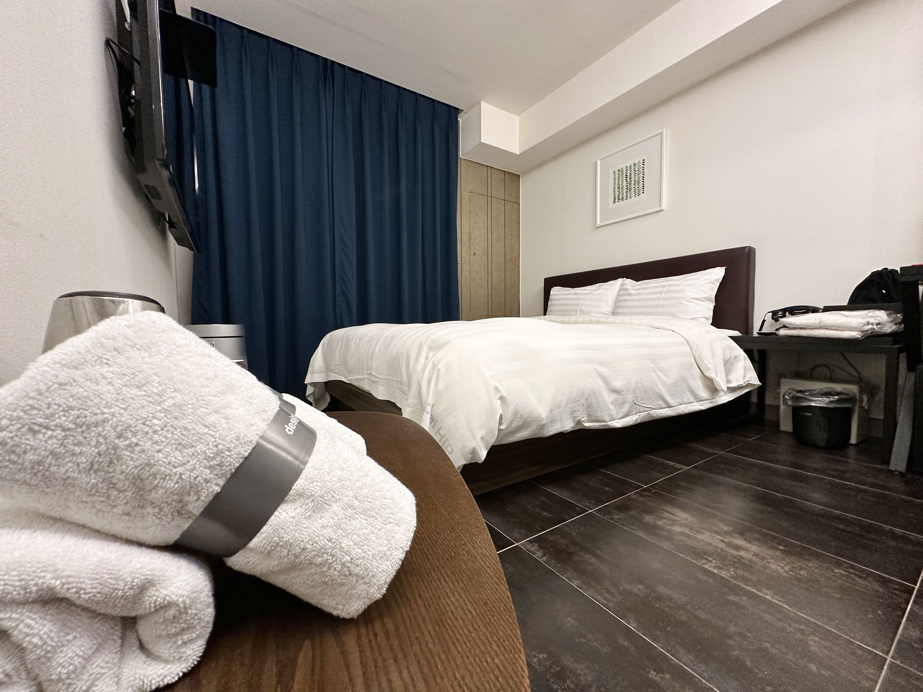 Habitación de hotel con cama, escritorio, cesto de basura y televisor montado en la pared.