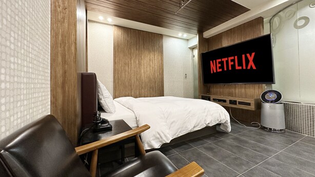 Una habitación de hotel moderna con una cama, un televisor mostrando 'NETFLIX', un escritorio y una silla.