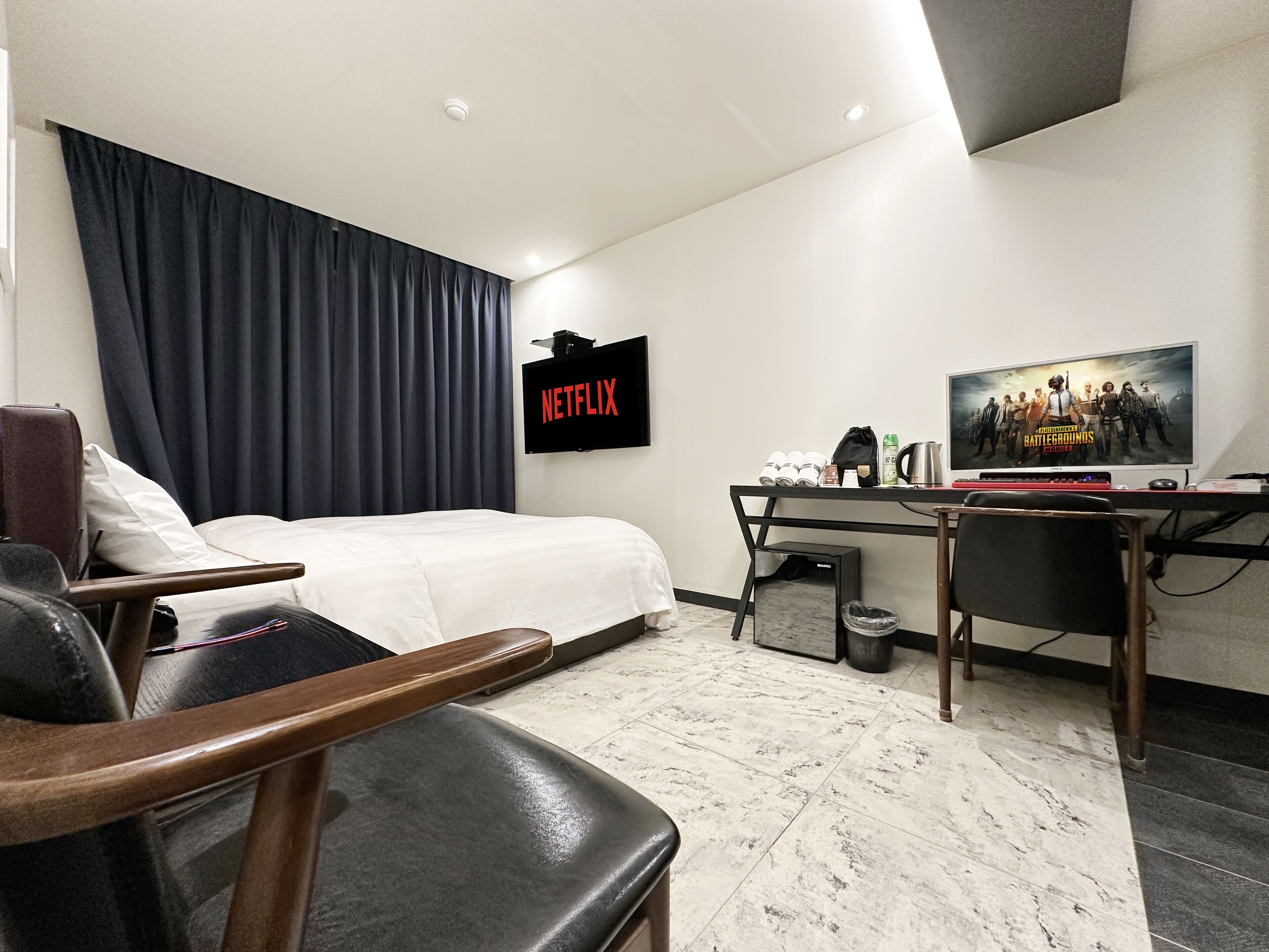 A modern hotel room with a bed, a desk, a chair, a TV, and a coffee machine.