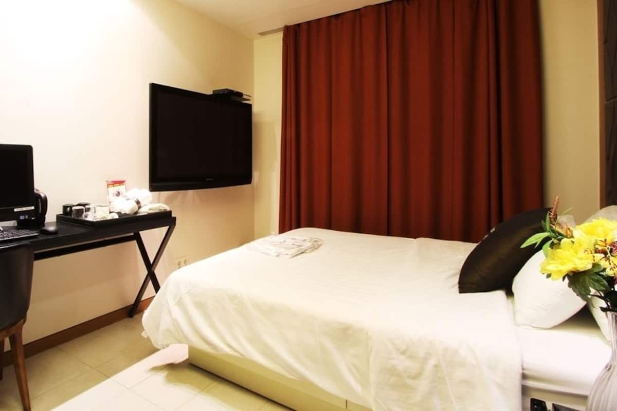 A hotel room with a bed, a desk with a computer, a TV, and a vase with flowers.