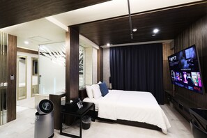 Una habitación de hotel moderna con cama, televisor montado en la pared, zona de ducha y una pequeña mesa con un control remoto.