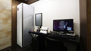 Habitación de hotel con minibar, escritorio con computadora, espejo y refrigerador.