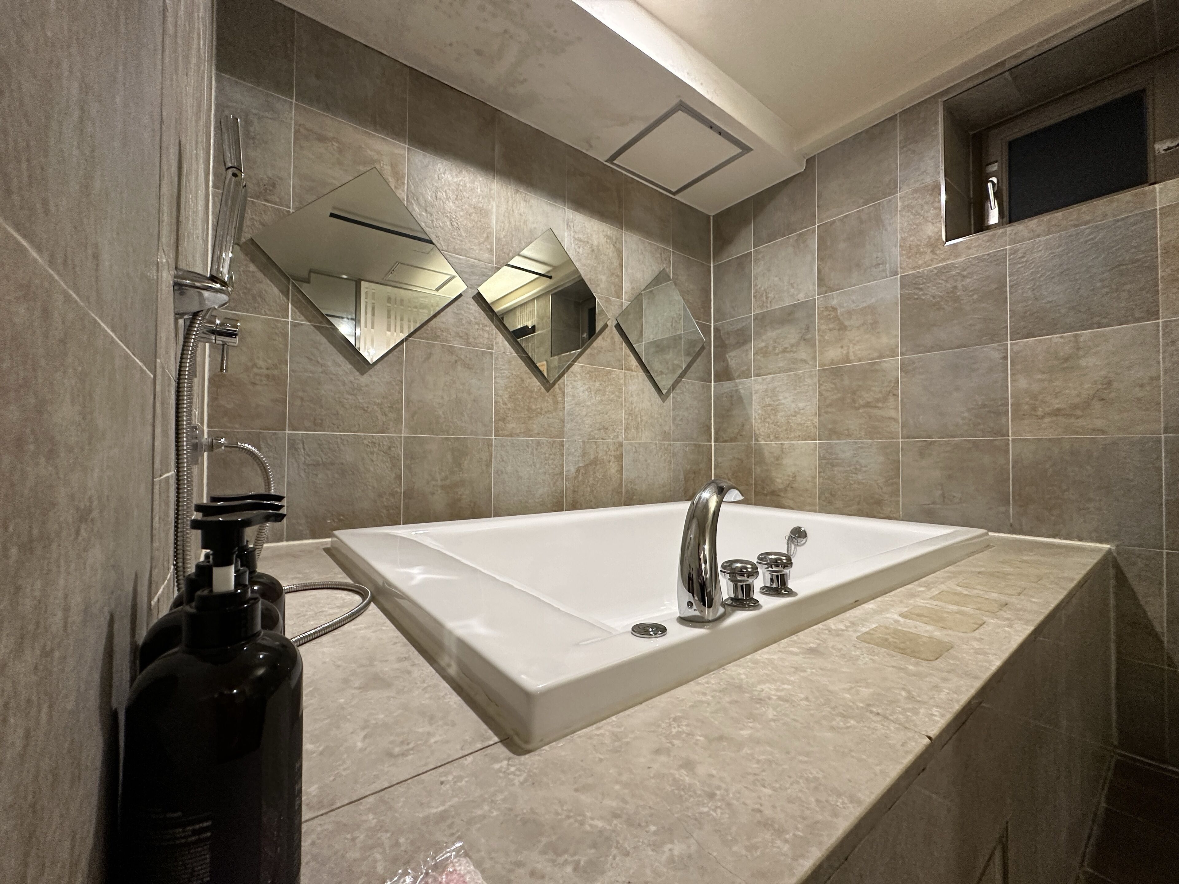 Un baño moderno con una bañera blanca grande, un cabezal de ducha manual y una botella de champú.