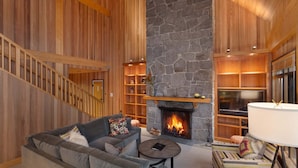 A cozy living room with a stone fireplace, a sofa, a coffee table, and a staircase. - Mountain townhouse w/ ski access & hot tub (Whistler)