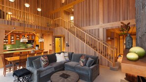 A spacious living area with a large gray sectional sofa, a wooden staircase, and a kitchen with wooden cabinets and a green countertop. - Mountain townhouse w/ ski access & hot tub (Whistler)