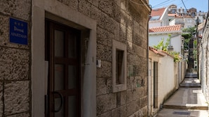 A narrow street with stone buildings, a visible door with a sign, and a clear sky.